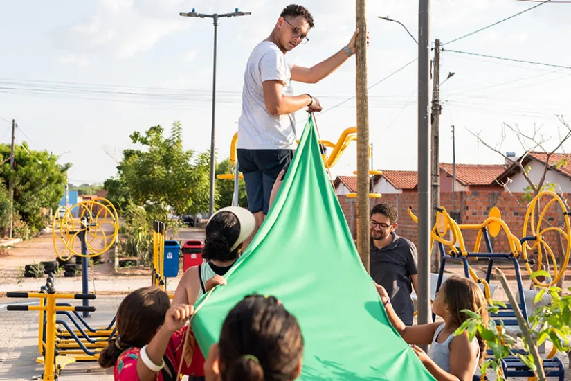 Unos niños ayudan a dos hombres a sujetar una sábana verde delante de un parque infantil en Teresina, Brasil.