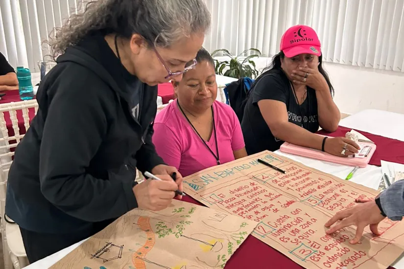 Three women write and draw on pieces of paper during a workshop.