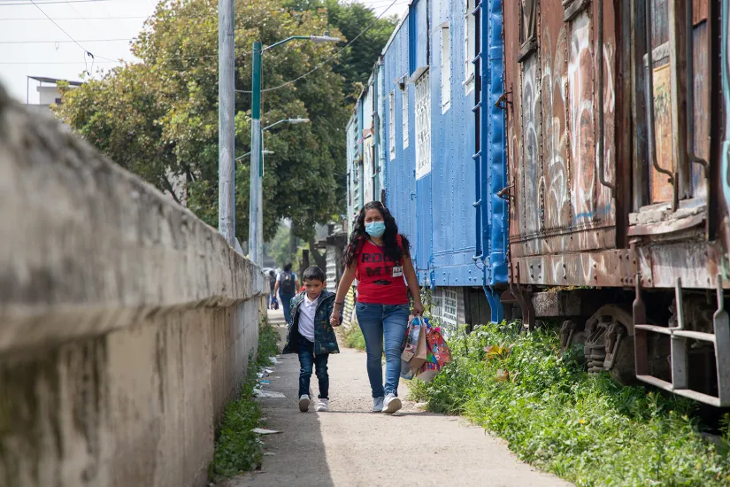 A woman with a small child walk along a path where next to it abonded train wagons are transformed into informal houses