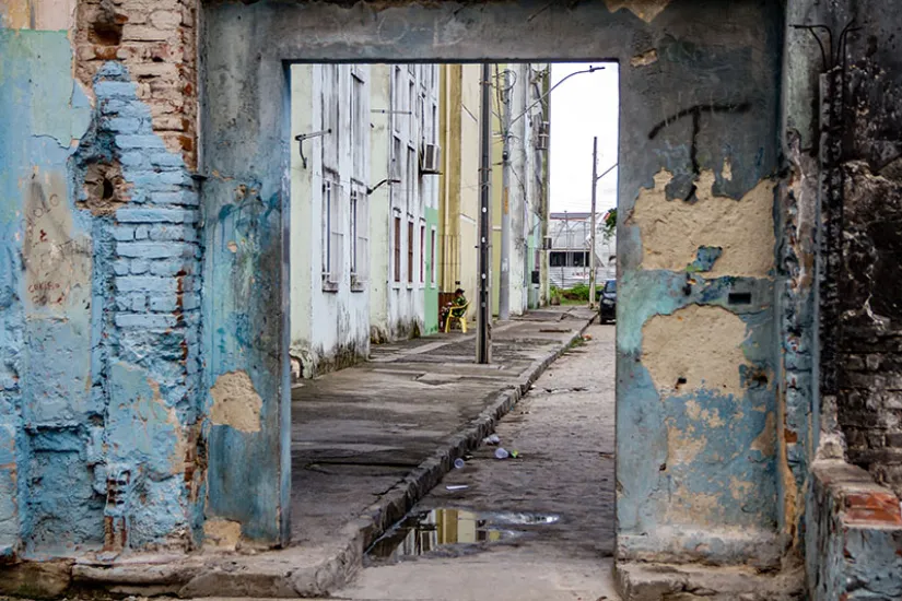 Um antigo portal proporciona uma visão de uma rua não pavimentada com calçadas pavimentadas em Recife, Brasil.