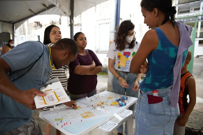 Um homem, quatro mulheres e uma criança estão em pé ao redor de uma mesa com um mapa.