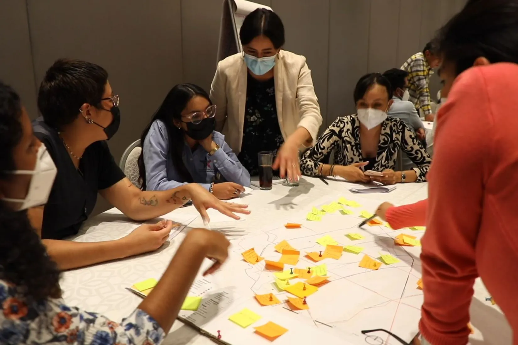 Miniatura de vídeo mostrando pessoas usando máscaras colando notas adesivas em um mapa disposto sobre uma mesa.