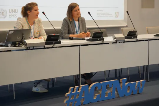 Two women sit behind a table with microphones in a conference room