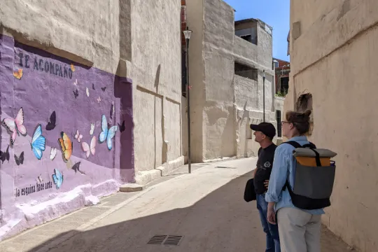 Mulher e homem olham para uma pintura mural de borboletas em um fundo roxo