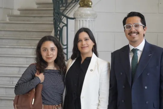 Three formally dressed people stand in a hallway