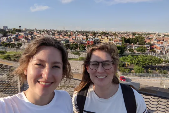 Two women take a selfie in front of a city.
