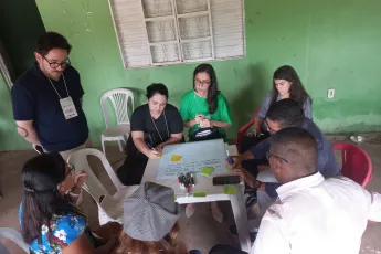 A group of people around a table are writing on a large sheet of paper.