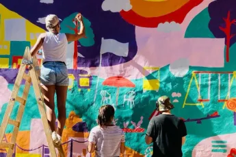 Duas mulheres e um homem pintando um mural em uma parede