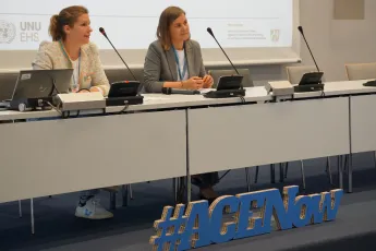 Two women sit behind a table with microphones in a conference room