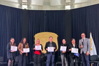 A group of seven people stand on a stage holding certificates