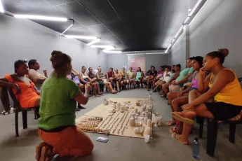 A group of women sit in a half circle around crafts layed out on a carpet.