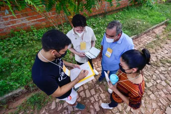 Four people look at a paper one of them is holding while standing outside in a street of cobble stones