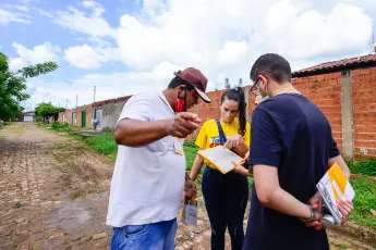 Quatro pessoas conversam em uma rua calçada com pedras enquanto olham para uma folha de papel que uma delas está segurando.