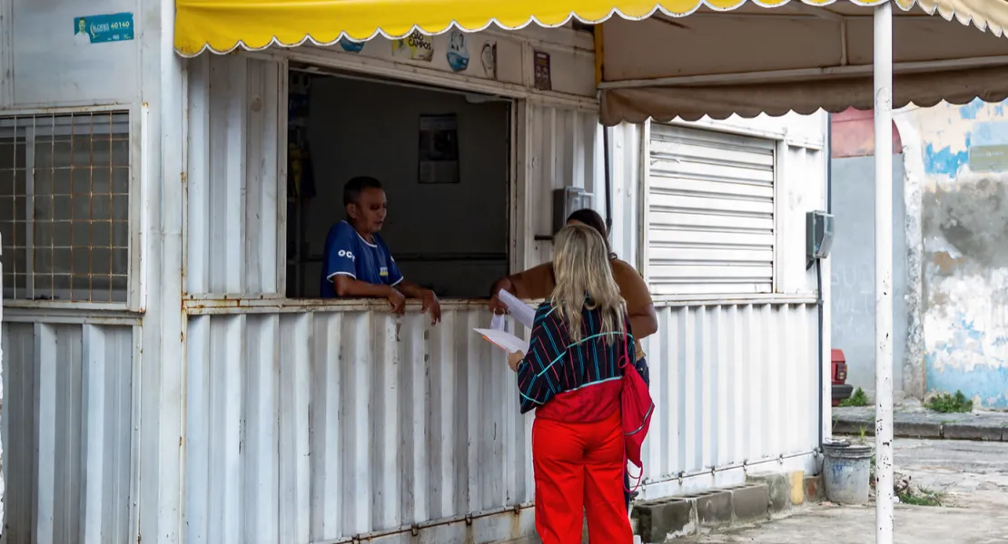 Two people stand under a plastic awning and talk to a man in a container that was transformed into a house