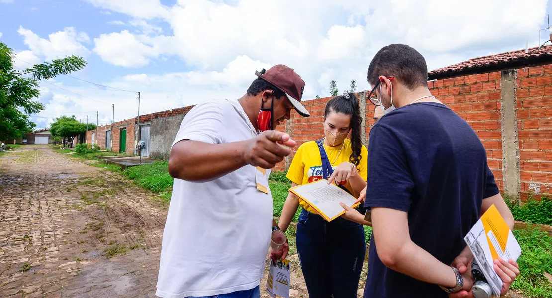 Quatro pessoas conversam em uma rua calçada com pedras enquanto olham para uma folha de papel que uma delas está segurando.